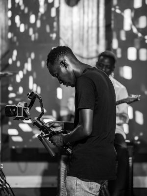 Candid black and white shot of a cameraman filming on set.